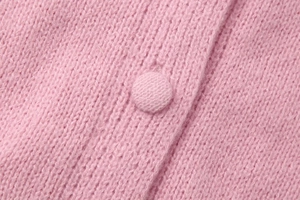 Macro shot of pink knit texture with matching fabric-covered button detail on cardigan