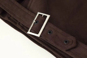 Macro detail of deep brown suede jacket featuring a silver metal buckle and eyelet strap