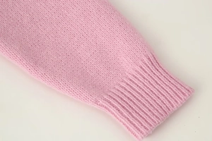 Detailed close-up of the ribbed cuff on a pink knitted cardigan showing texture