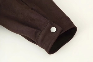 Detail shot of a dark brown suede jacket cuff with a silver metal button on a light background
