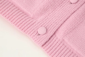 Detail of pink knit cardigan showing fabric texture, ribbed hem and matching fabric buttons