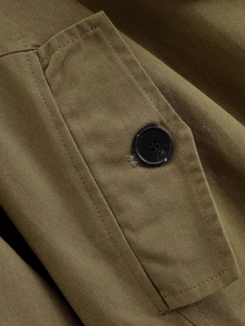 Detailed close-up of trench coat epaulette with black button and khaki twill fabric texture
