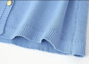 Detailed close-up of light blue knit fabric featuring ribbing and a gold button