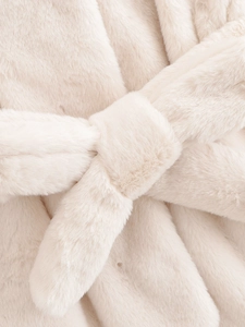 Detail of soft cream faux fur texture and matching waist tie bow on the winter coat