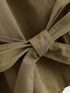 Detail of waist tie bow and twill fabric texture on a women's khaki trench coat