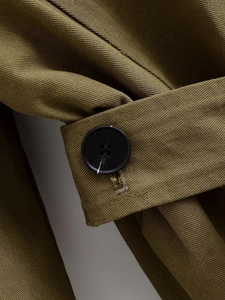 Macro detail of olive green twill fabric and black four-hole button on the trench coat sleeve