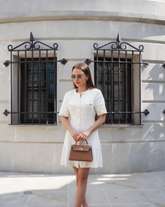 Detail of white knitted short sleeve dress showing golden buttons and textured fabric
