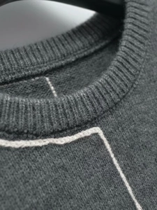 Detail of grey knitted sweater showing ribbed crew neck and white contrast stitching