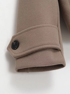 Detailed view of camel wool coat cuff with adjustable strap and black button texture