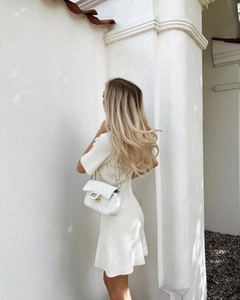 Detail of white ribbed knit dress and quilted shoulder bag with gold chain strap