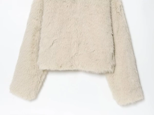 Close-up detail of soft beige faux fur texture on a short winter coat for women