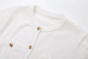 Close-up of white knit dress with ribbed collar and embossed golden metal buttons