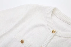 Detail of white knit dress neckline with elegant gold embossed crest metal buttons