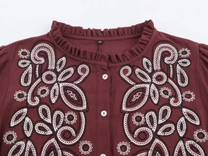 Detailed close-up of bohemian floral embroidery and ruffled collar on burgundy shirt