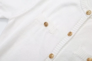 Detail of white knit cardigan showing vintage gold relief buttons and ribbed edge texture
