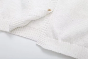Close-up of white knitted dress fabric featuring a shiny gold button and ribbed hem detail