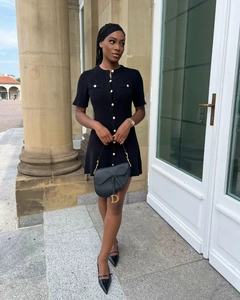 Detail of short sleeve knit dress with gold buttons and a stylish black saddle bag