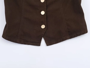 Dettaglio dell'orlo in twill marrone scuro con taglio a V e bottoni in metallo dorato