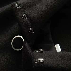 Detail of silver metal hook-and-eye closures and decorative ring on black wool coat