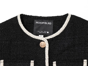 Détail macro du col rond d'une veste en tweed noir avec bordure tissée blanche et bouton doré