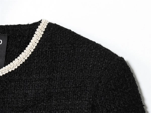 Détail du col d'une veste en tweed noir avec bordure tissée blanche et texture riche