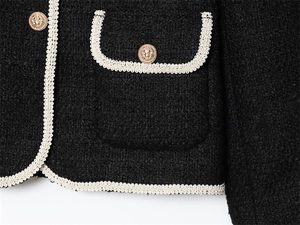 Vue détaillée du tissu en tweed noir avec boutons de lion dorés et finitions tressées
