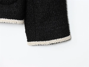 Détail de la veste en bouclé noire montrant la texture élégante de la bordure tressée