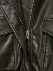 Detailed macro view of olive green PU leather jacket showing metallic zipper and flap pockets