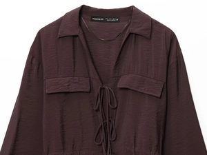 Detail of dark brown long-sleeve shirt featuring bow-tie collar and double chest pockets