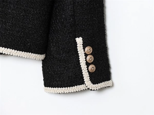 Gros plan sur la veste en tweed noir avec boutons dorés et détails de bordure tissée blanche