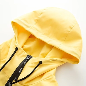 Detail of yellow waterproof hooded jacket featuring black drawstrings and branded zipper puller