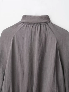 Detail of grey standing collar jacket showing fabric texture and pleat craftsmanship