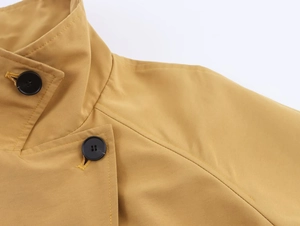 Detail of mustard yellow trench coat collar featuring black buttons and stitching