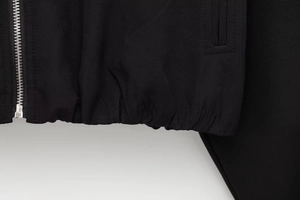 Detail of a black jacket featuring silver metal zipper and elastic ribbed hemline