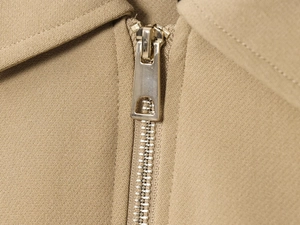 Detailed close-up of premium metal zipper and khaki woven fabric on women's jacket