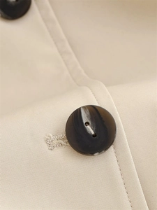Detailed macro view of high-quality twill fabric and marbled resin button on short trench coat