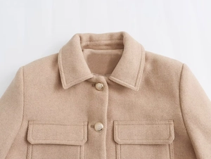 Detailed close-up of beige wool jacket featuring golden metal buttons and symmetrical chest pockets