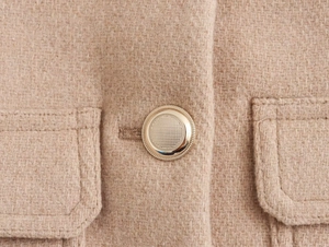 Detailed macro view of khaki wool coat featuring a golden metal button and stitched pocket