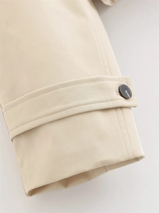 Close-up of beige trench coat sleeve cuff with grey button and refined stitching details