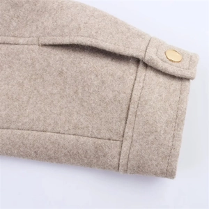 Close-up of soft oatmeal wool jacket pocket featuring a polished gold button detail