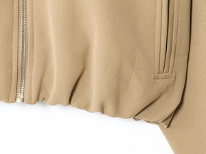 Detail shot of khaki puffy jacket hem with metal zipper and reinforced side pocket