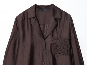 Close-up of dark brown silk-like shirt pocket featuring intricate scroll embroidery detail