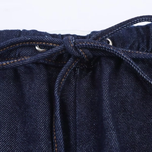 Detail of high-waist denim pants featuring an elastic waistband with drawstring and metal eyelets