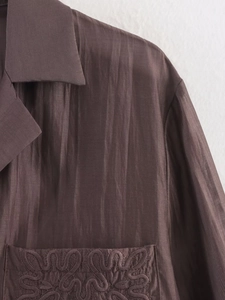 Macro detail of silk-like chocolate brown shirt collar and elegant pocket embroidery