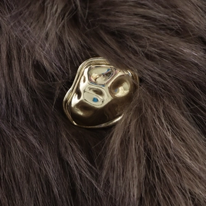 Bouton métallique doré irrégulier style lave sur manteau de fourrure au fini brillant