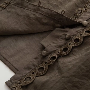 Macro shot of brown lace trim shirt featuring fabric buttons and geometric embroidery detail