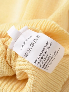 Detail of white clothing care label on 100% polyester yellow knit top showing washing symbols