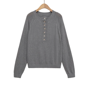 Détail d'un pull en maille gris foncé avec des boutons décoratifs sur la couture de l'épaule