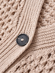 Makroaufnahme der beigen Strickweste mit Waben-Häkelmuster und einem schwarzen Knopf
