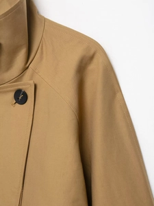 Detail of khaki cropped trench coat showing stand collar and raglan sleeve construction